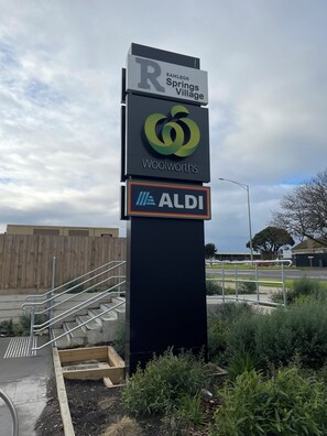 Een bord met de logo's van Woolworths en ALDI, een houten hek en een metalen trap.