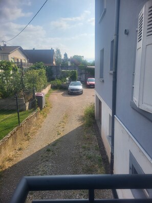 A residential street with two parked cars, a gravel driveway, and a fence.