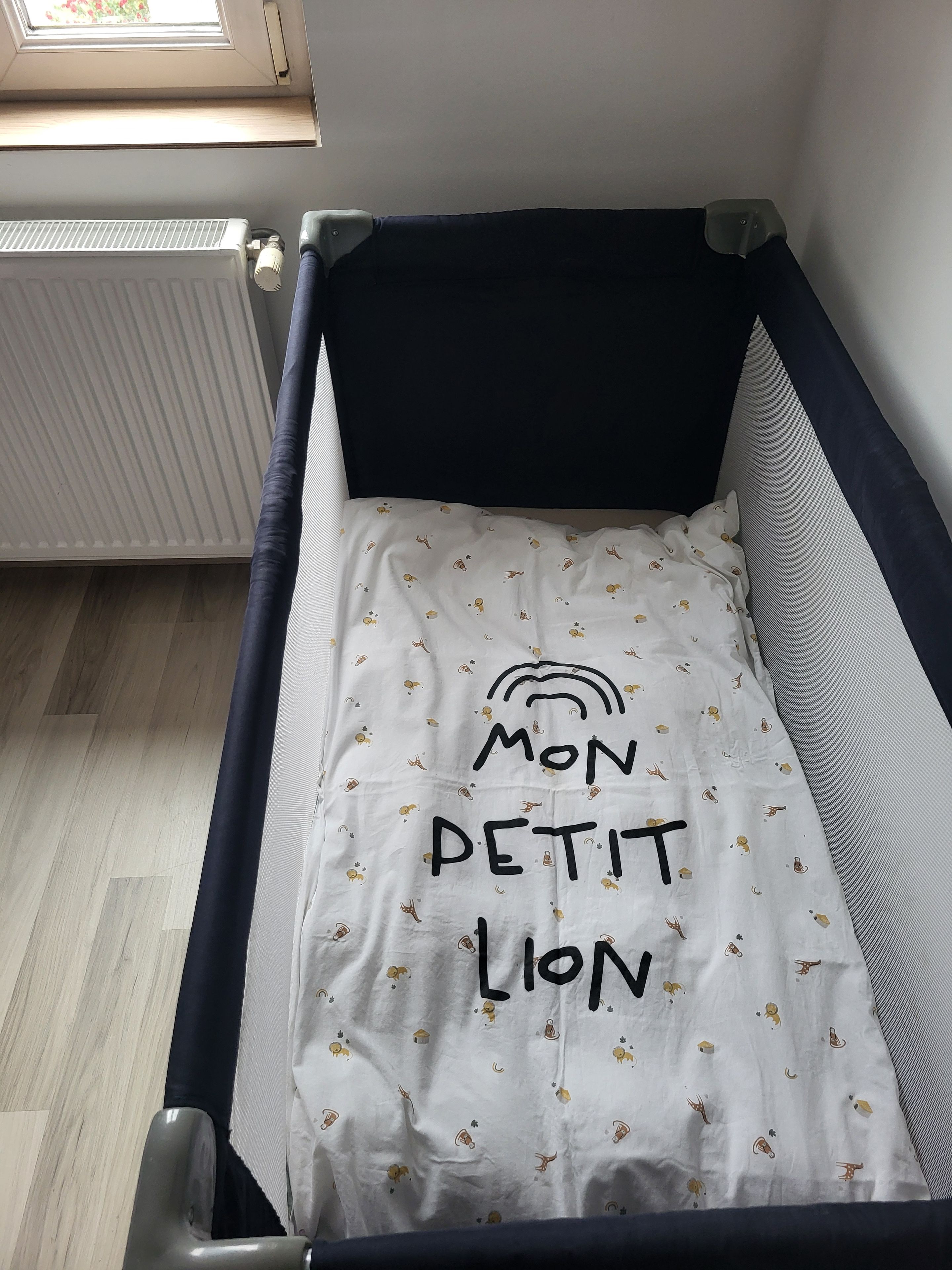 Una cuna para bebé con colchón blanco, estampado de león y la inscripción 'Mon Petit Lion'.