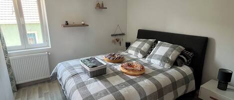 A bedroom with a bed, a bedside table, a hanging light fixture, a window, and a radiator.