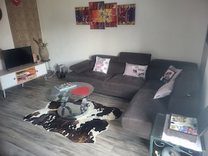 Ein Wohnzimmer mit einer Couch, einem Glastisch, einem Fernseher und einem Teppich.
