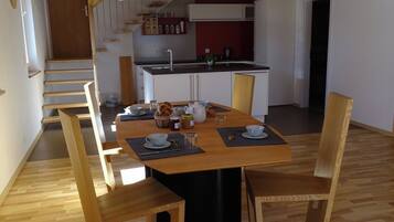 A dining area with a wooden table, chairs, and a kitchen in the background.