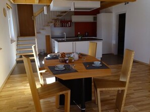Ein Essbereich mit einem Holztisch und Stühlen, eine Küche im Hintergrund und eine Treppe, die in eine andere Ebene führt.