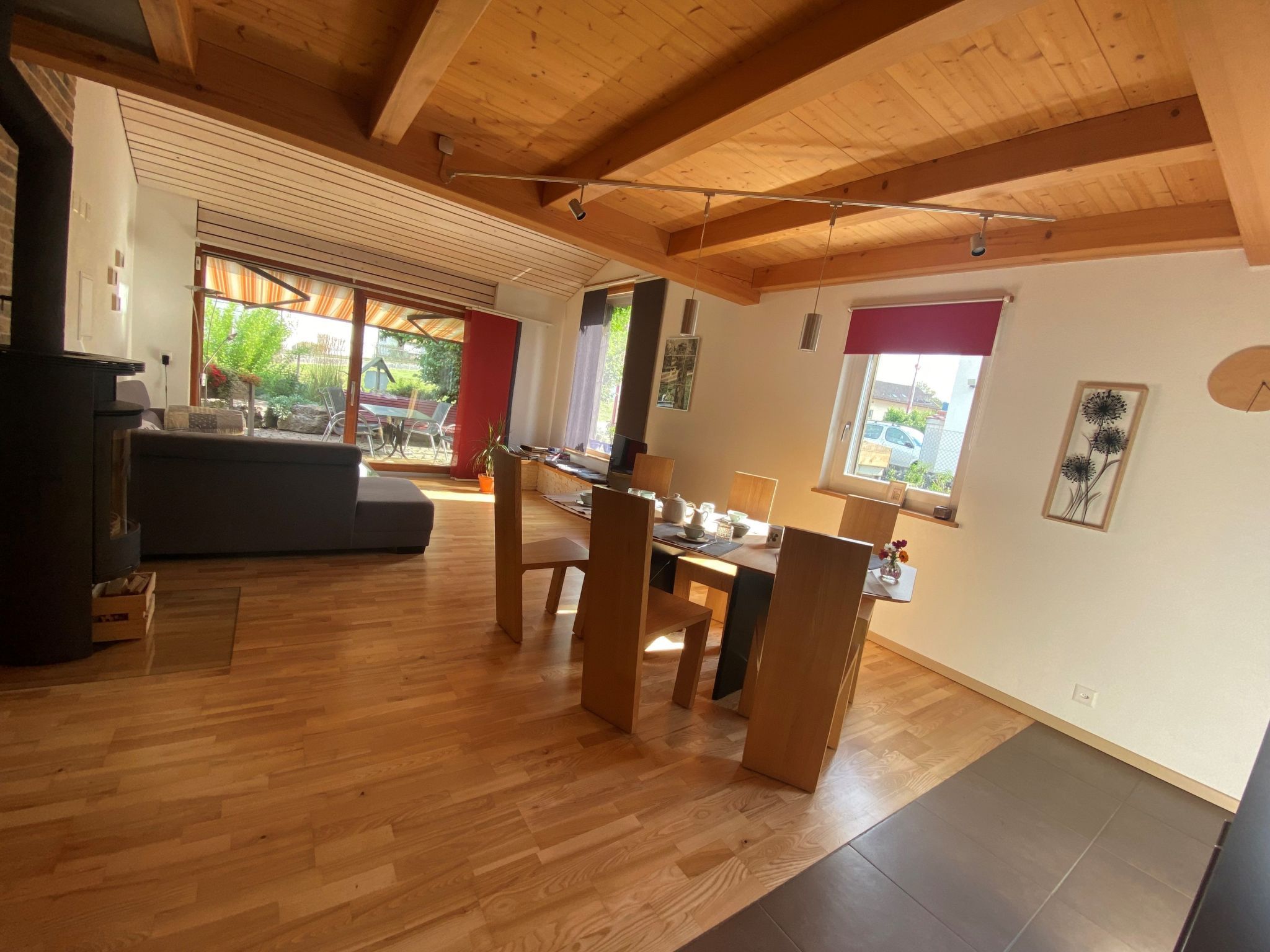 Ampla sala de estar com teto de madeira, mesa de jantar com cadeiras e uma grande janela com vista para o exterior.