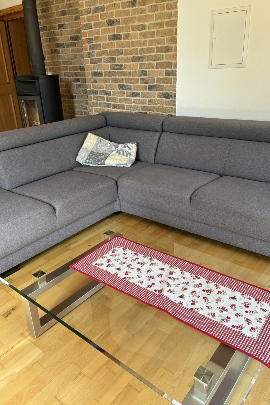 A modern living room with a grey sectional sofa, a patterned rug, and a brick wall.