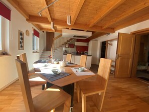 A dining area with a wooden table, chairs, and a kitchen in the background. - Appartement - La Racrue, (Lajoux JU), by Interhome (Lajoux JU)