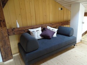 A wooden ceiling, a sofa with cushions, and a white vase on a wooden bench. - Appartement - La Racrue, (Lajoux JU), by Interhome (Lajoux JU)