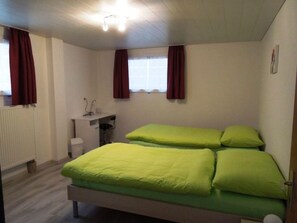 A bedroom with a bed, a radiator, a window with curtains, and a small desk with a chair.