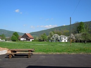 A rural landscape with a wooden bench, a white building with a red roof, and a clear blue sky.