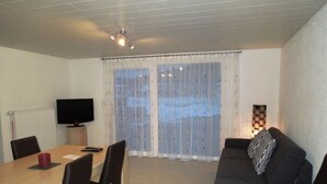 Een moderne woonkamer met een eettafel, stoelen, een bank, een televisietoestel en een raam met gordijnen.