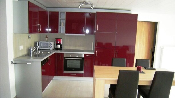 Een moderne keuken met rode kastjes, een magnetron, een koffiezetapparaat en een eettafel met stoelen.