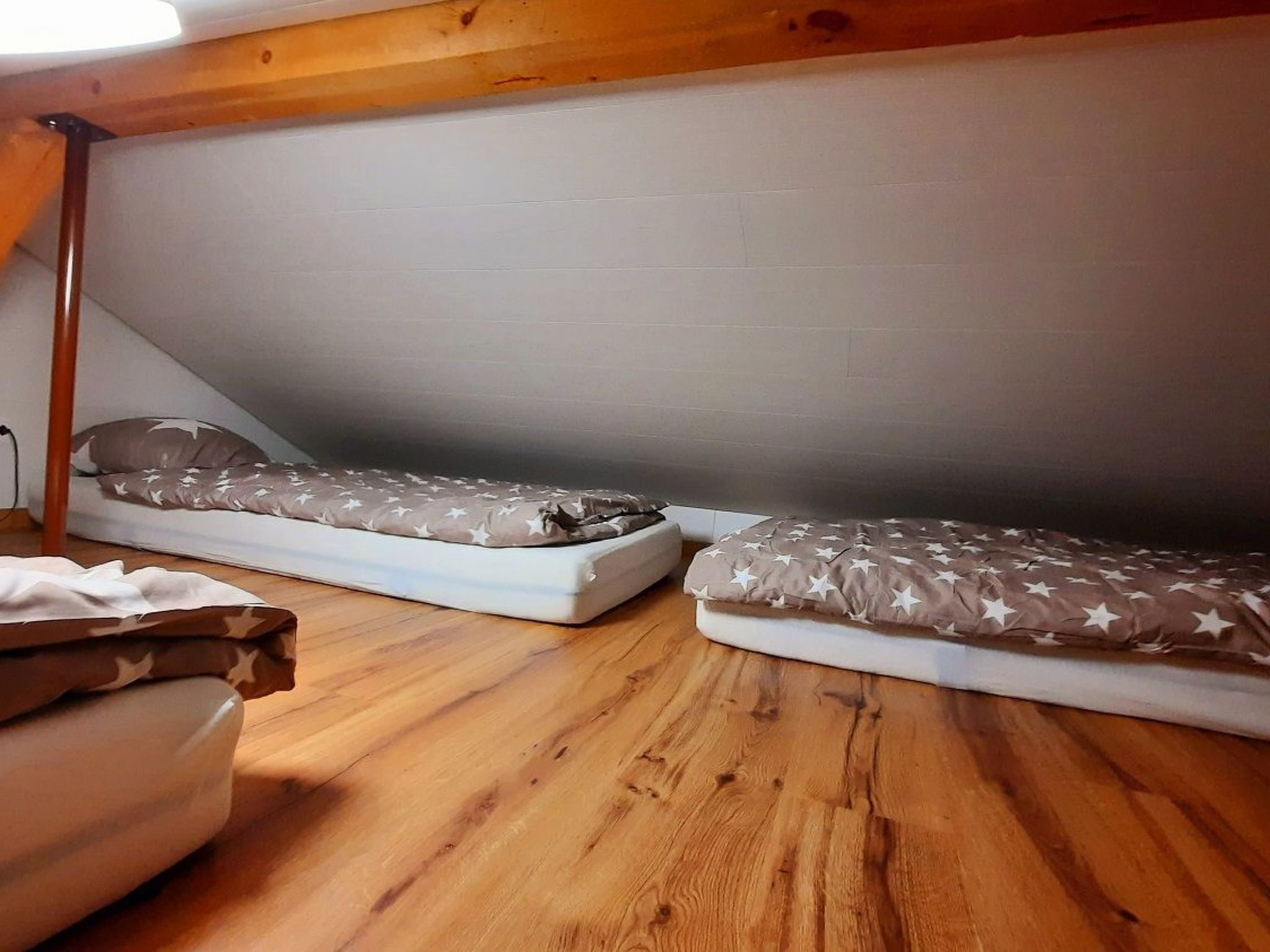 Une petite pièce fermée, avec deux lits superposés, un plancher en bois et un plafond en pente.