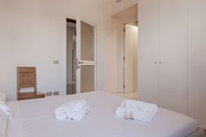 A clean, modern hotel room with a large bed, two rolled towels, a wooden nightstand, and a wardrobe. - Domio Fly & Drive | Urban Chic with A/C (Bergamo)