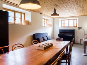A dining area with a long wooden table, chairs, a sofa, and a piano. - Appartement - Gîte chez MarEdo, (Montmelon), by Interhome (Montmelon-St.Ursanne)