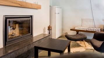 A modern living room with a fireplace, a table, a sofa, and a refrigerator.