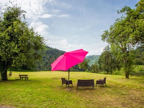 An outdoor seating area with a table and chairs under a pink umbrella, surrounded by trees and a grassy field. - Appartement - Gîte chez MarEdo, (Montmelon), by Interhome (Montmelon-St.Ursanne)
