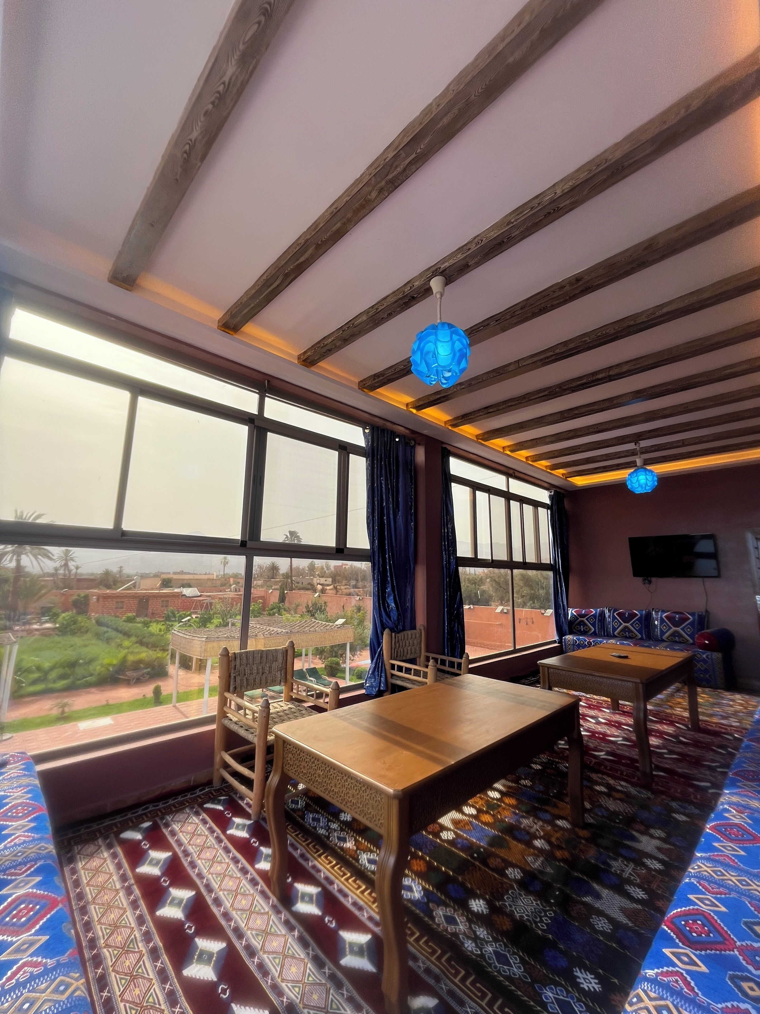 A room with a large window, a wooden ceiling, a patterned carpet, and a table with chairs.