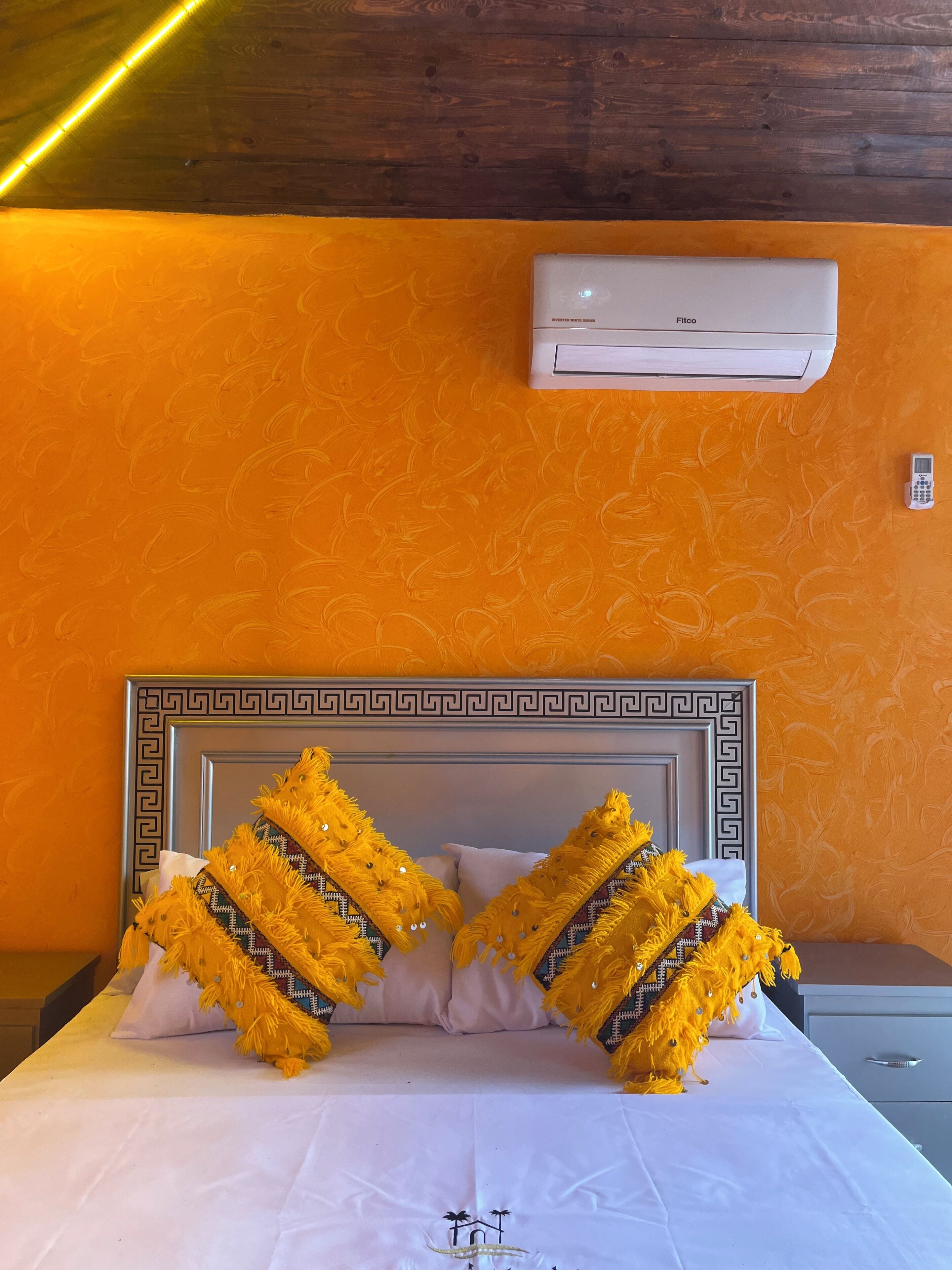 A hotel room with a bed, an air conditioner, and a bedside phone.