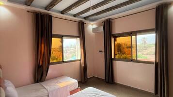 Una camera d'albergo con due letti singoli, un soffitto a vista con travi e ampie finestre con tende.