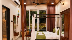 Una cama con dosel y cortinas, un ventilador de techo de madera y vistas a un jardín a través de un ventanal.