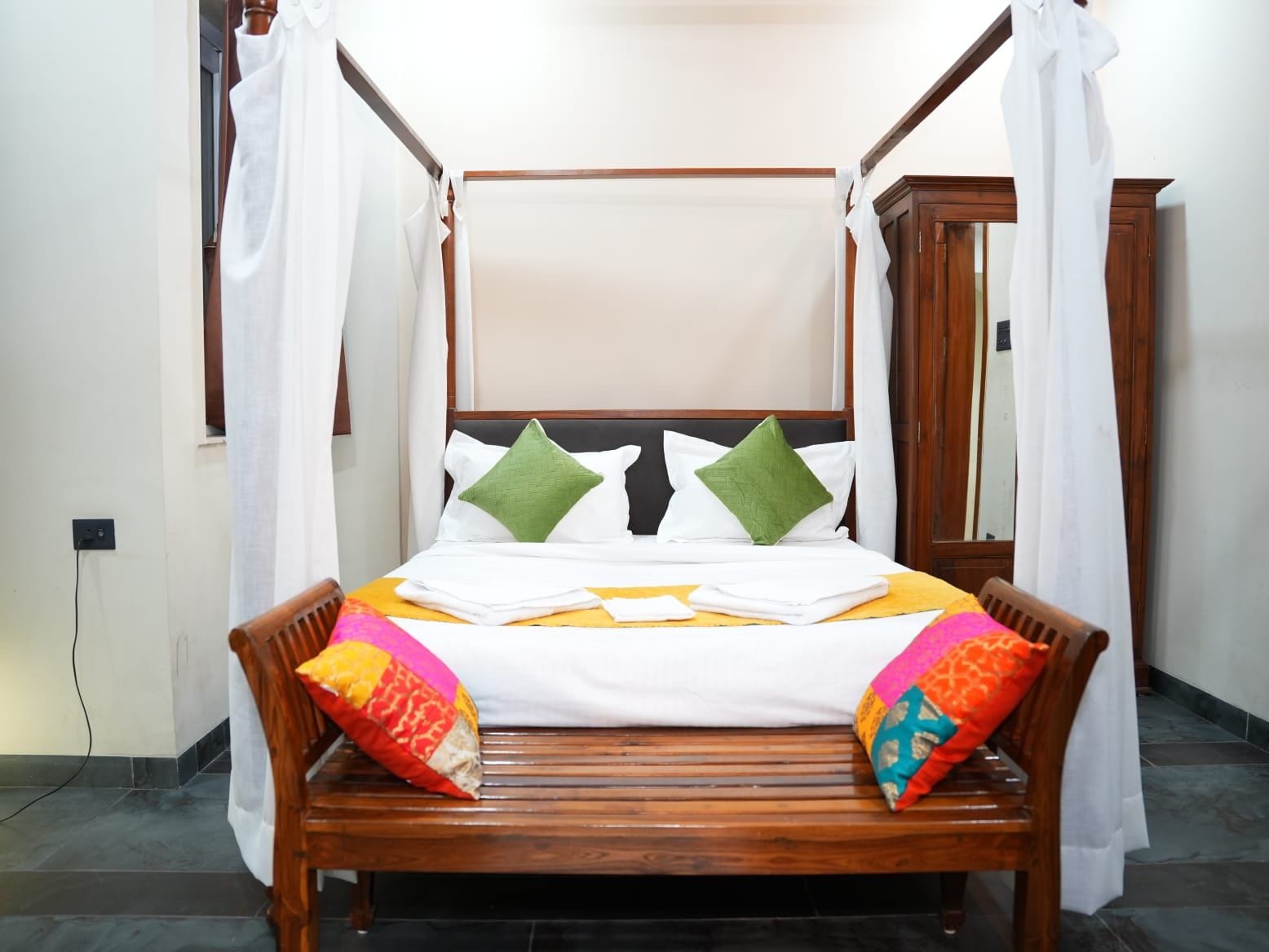 A four-poster bed with white linens and green pillows, a wooden headboard, and a yellow bedspread.