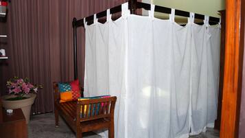 Um quarto com um banco de madeira, uma cama com dossel branca, um vaso de planta e uma prateleira fixada na parede.