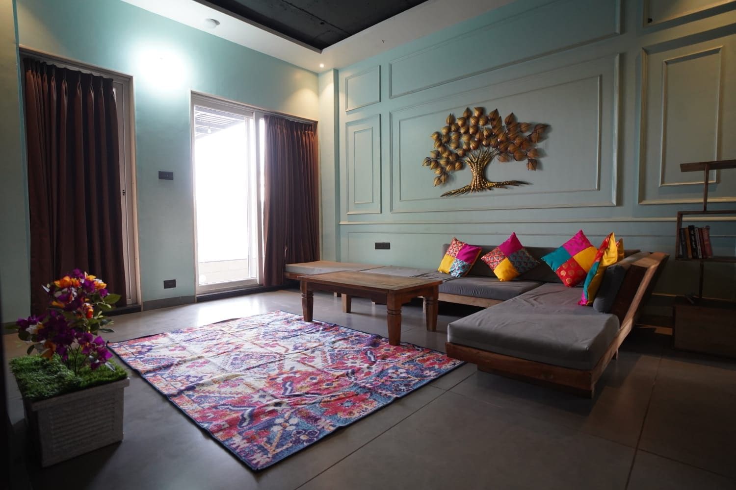Una sala de estar con sofá, una mesa de centro, un tapete y un elemento decorativo de pared con motivos de árbol.