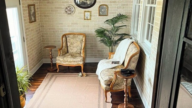 A cozy room with a brick wall, wooden beams, a chandelier, two armchairs, a small table, and a potted plant. - The Claxton house a Greenup county Historic home built in 1864 with hot tub (Greenup)