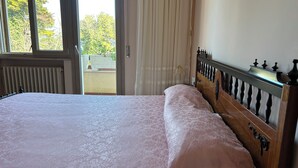 Un dormitori amb un llit, una finestra, un radiador i vista a l'exterior.