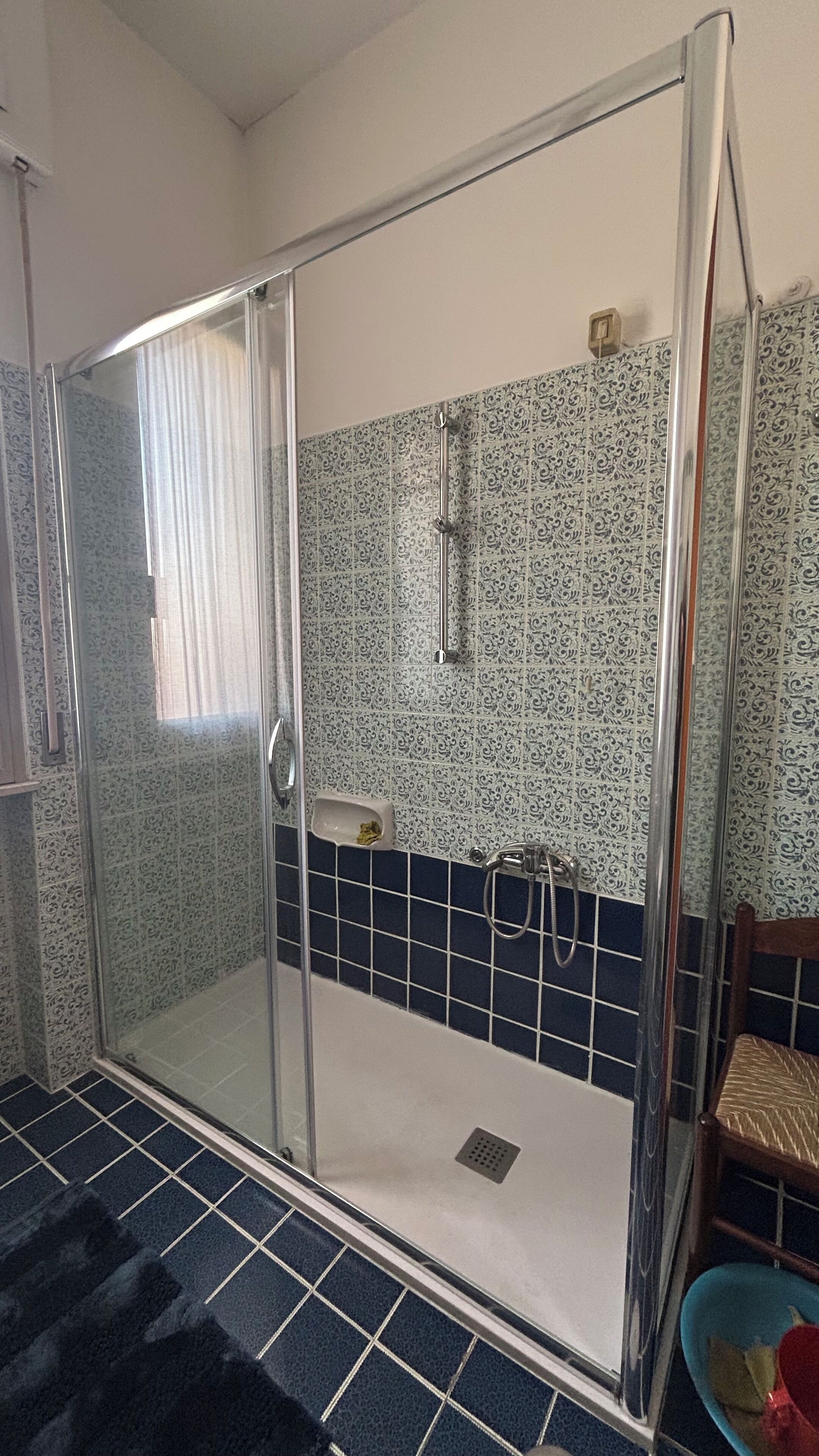 Un área de ducha con puerta de vidrio, alcachofa y pared con azulejos.