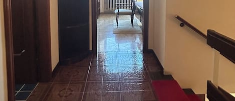 A hallway with patterned flooring, a red carpet, a wooden bench, and a door leading to a balcony.