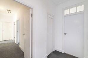 A hallway with white doors, carpeted flooring, and a ceiling light fixture. - Spacious & Stylish 4-Bed Flat in Golders Green - Pass the Keys (London)