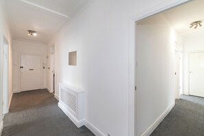 A hallway with white walls, a radiator, and a door at the end. - Spacious & Stylish 4-Bed Flat in Golders Green - Pass the Keys (London)