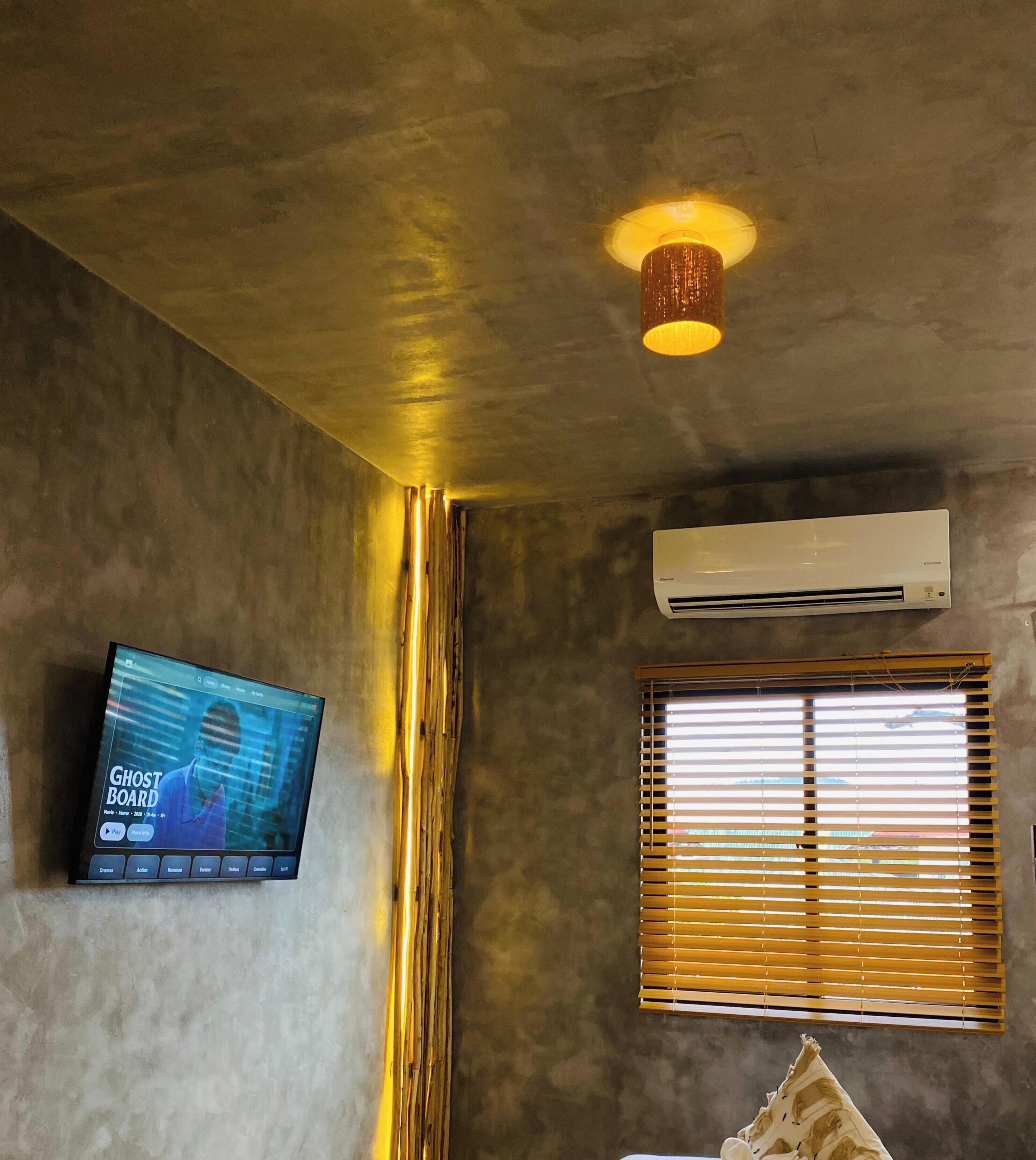 A room with a television displaying a movie, an air conditioning unit, and a window with blinds.