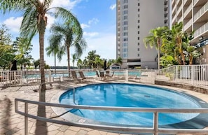 A swimming pool with lounge chairs and palm trees, surrounded by a tall building. - Spacious 2-bedroom condo with Lakeview in superb Orlando location Close 2 Disney (Orlando)