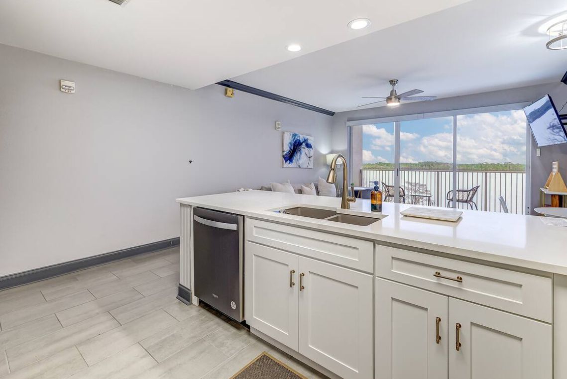 A modern kitchen with white cabinetry, a dishwasher, and a large window offering a view of the outdoors.