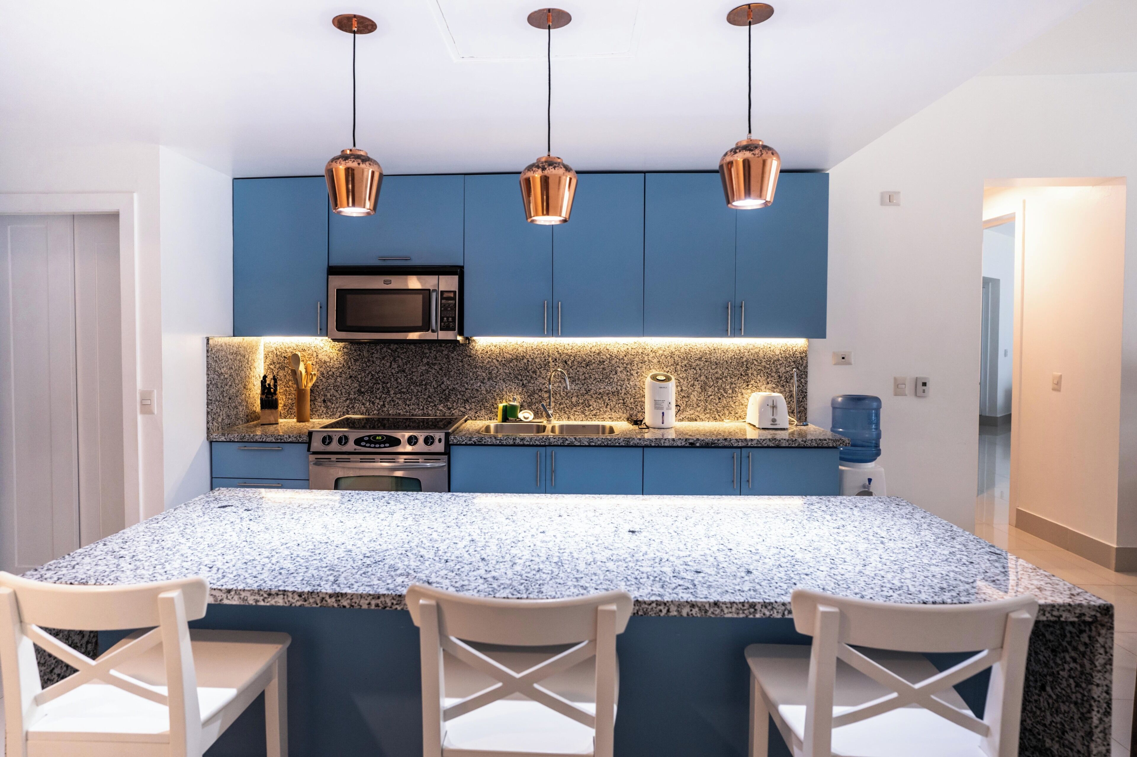 Uma cozinha moderna com armários azuis, bancada de granito, micro-ondas, fogão e três luminárias pendentes.