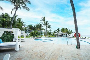A pool area with lounge chairs, a cabana, and palm trees. - SeaWinds Seaside Escape Spacious Condo (Cabarete)