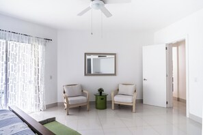 A spacious room with a bed, two armchairs, a small table with a plant, a ceiling fan, and a door. - SeaWinds Seaside Escape Spacious Condo (Cabarete)