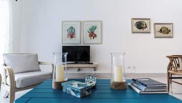 Uma sala de estar com uma mesa de centro azul, duas ilustrações emolduradas de peixes, um sofá, uma televisão e uma estante.