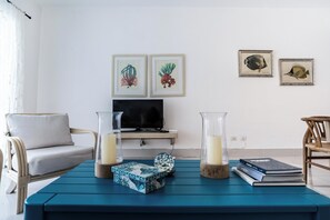 A living room with a blue coffee table, two framed fish illustrations, a sofa, a TV, and a bookshelf. - SeaWinds Seaside Escape Spacious Condo (Cabarete)