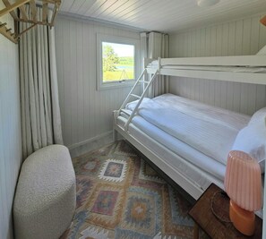 Ein Schlafzimmer mit Etagenbett, Fenster, Vorhängen, einem gemusterten Teppich und einem Sessel.