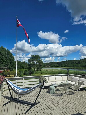 Eine Terrasse mit einer Hängematte, Gartenmöbeln und einer Fahnenstange mit einer Flagge.