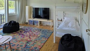 A room with a bunk bed, a television on a wooden stand, a desk with a chair, a colorful rug, and a large window with curtains. - Cabin with views over Hvaler archipelago (Gamle Frederikstad)