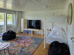 A room with a bunk bed, a television on a wooden stand, a desk with a chair, a colorful rug, and a large window with curtains. - Cabin with views over Hvaler archipelago (Gamle Frederikstad)