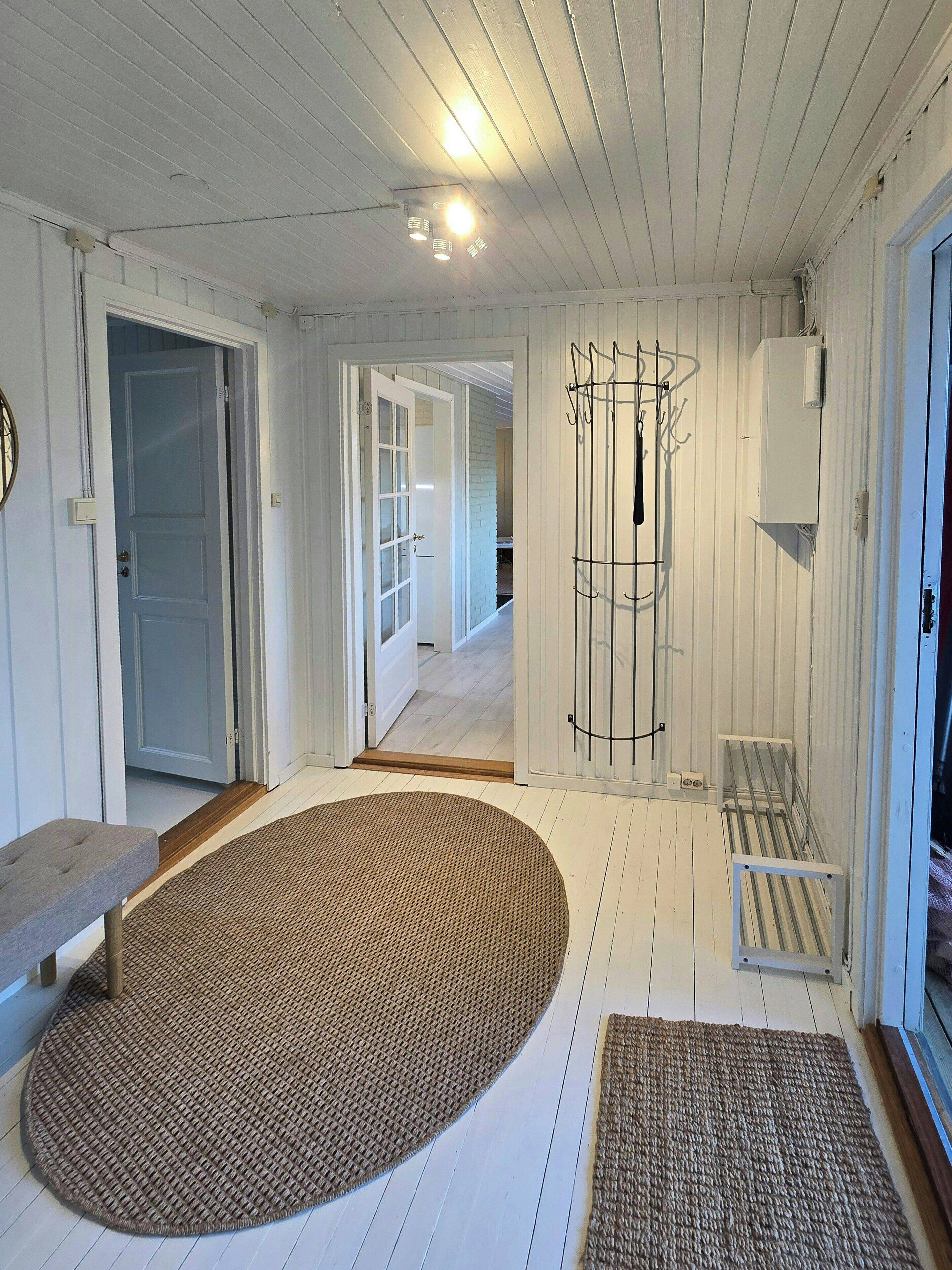 A room with a large woven rug, a bench, and a metal rack against the wall.