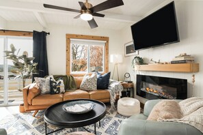 A living room with a sofa, a coffee table, a fireplace, a television, and a ceiling fan. - Charming 4-bedroom house with AC in Boyne Falls (Boyne Falls)