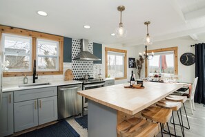 A modern kitchen with a central island, wooden bar stools, a built-in oven, and a large window. - Charming 4-bedroom house with AC in Boyne Falls (Boyne Falls)