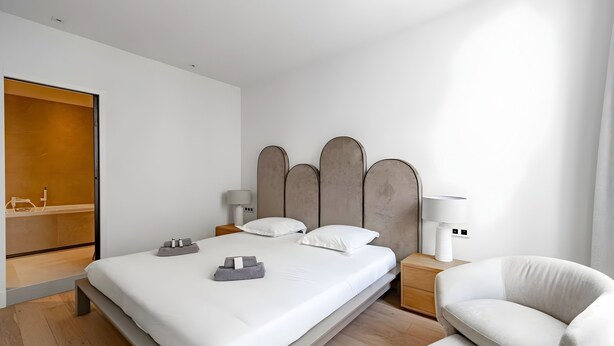 Et moderne hotelværelse med en stor seng, sengeborde, en stol og en sengegavl i træ.