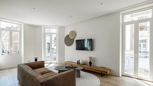En moderne stue med sofa, sofabord, tv ophængt på væggen og et stort vindue med udsigt over byen.
